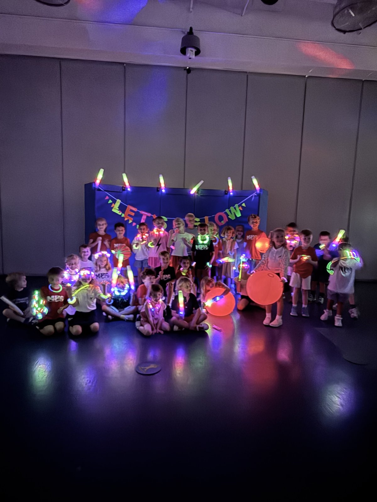 Students gathered on the stage under the Let's Glow banner at the MPA Glow Party