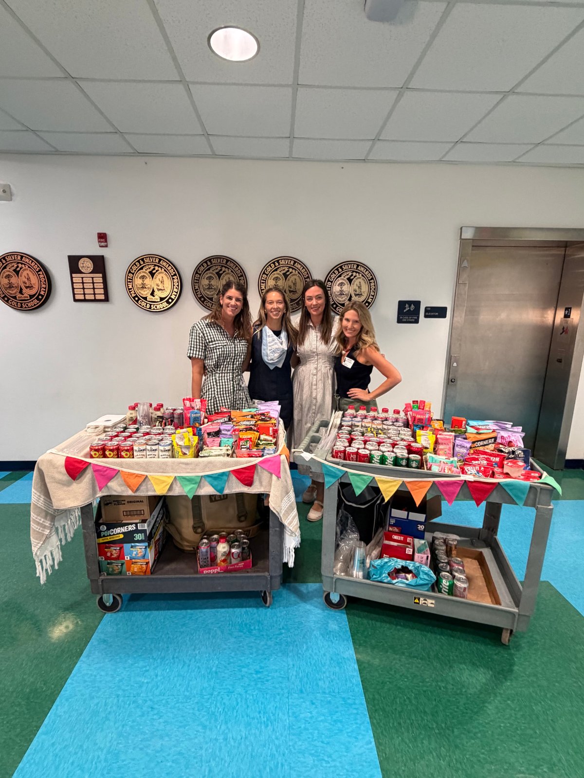 PTA volunteers standing behind two Snack Carts stocked with treats in the school hallway