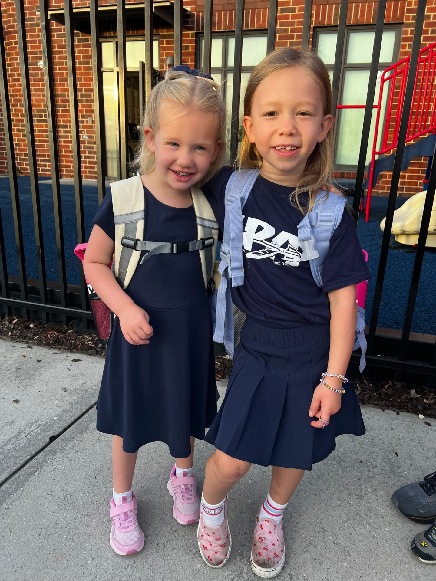 Two young MPA students with backpacks smiling outside the school gate
