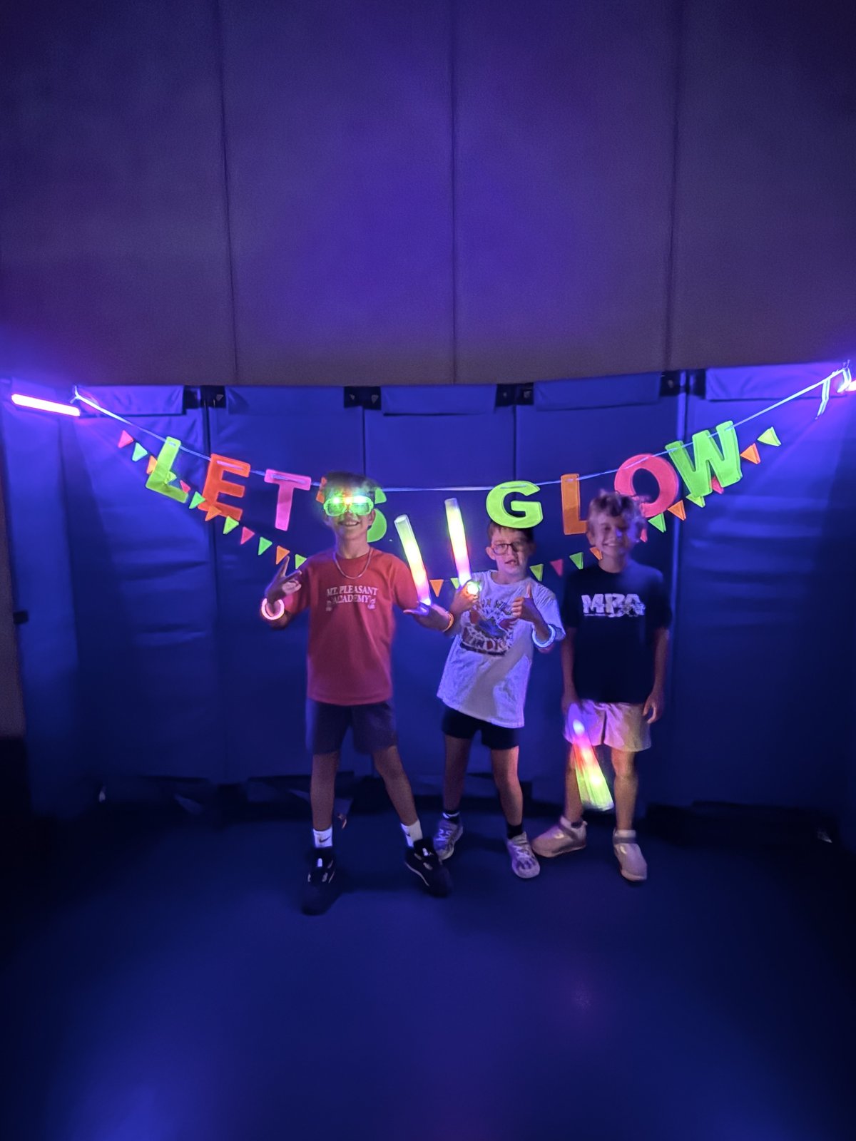 A crowd of MPA students glowing under the Let's Glow banner