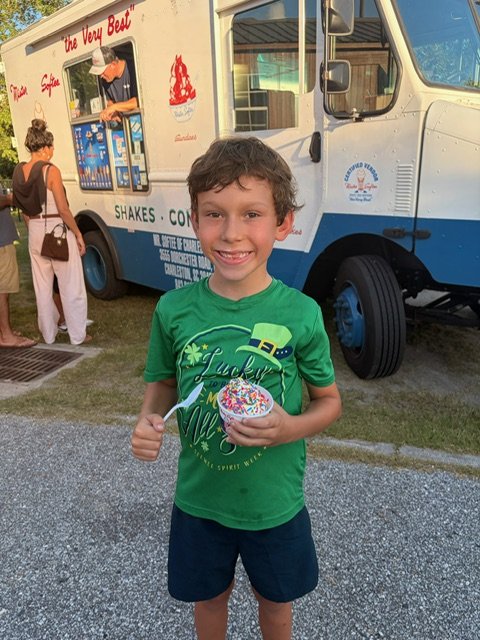 A student holding an ice cream cone in front of the Mister Softee truck