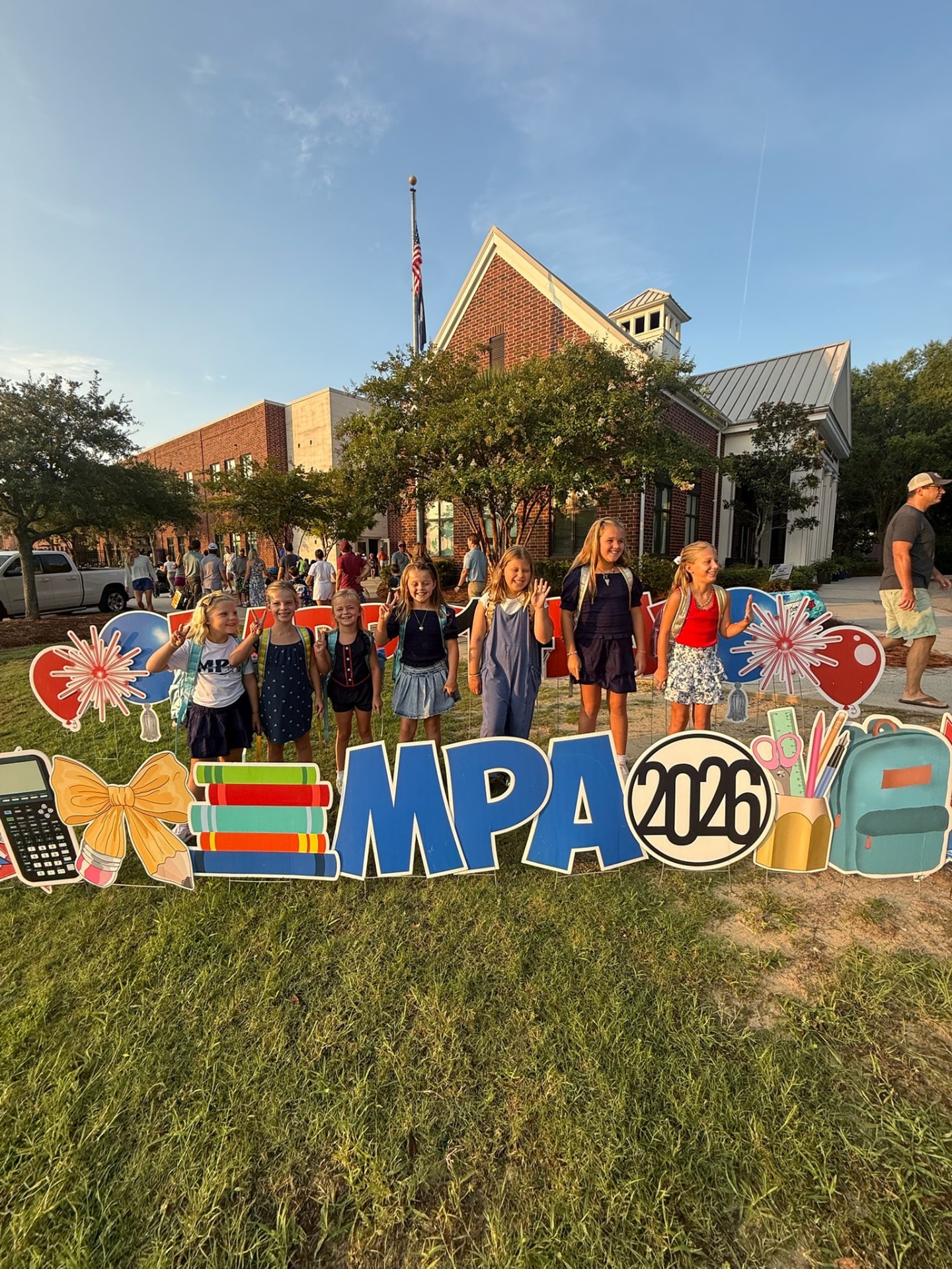 MPA students waving beside a colorful Welcome Back MPA 2026 yard sign display outside the school